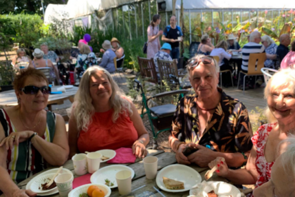 3 guests at table smiling with other tables, plants and polytunnels in background