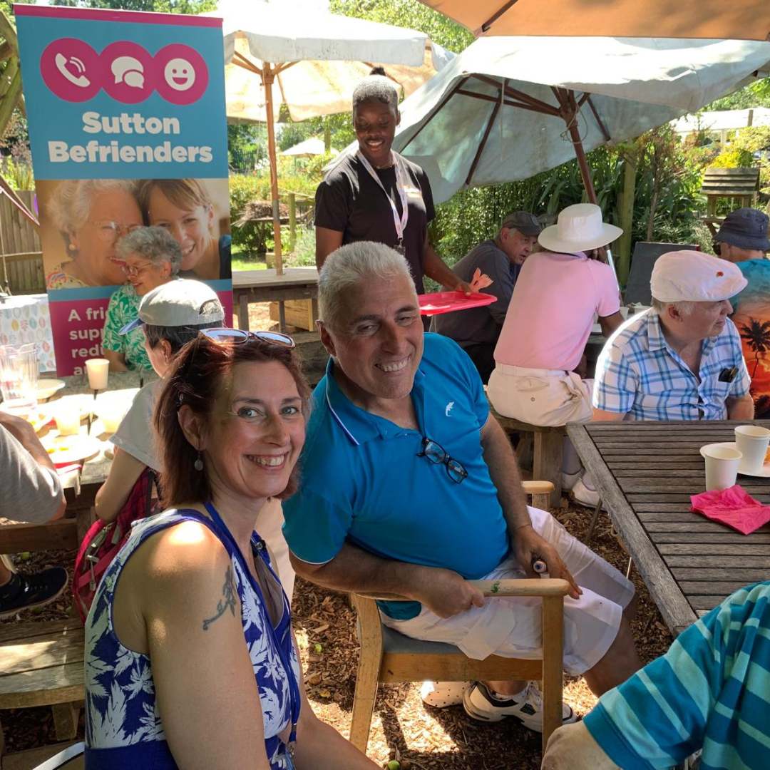 Group scene of people sat at tables with Sutton Befrienders banner in background