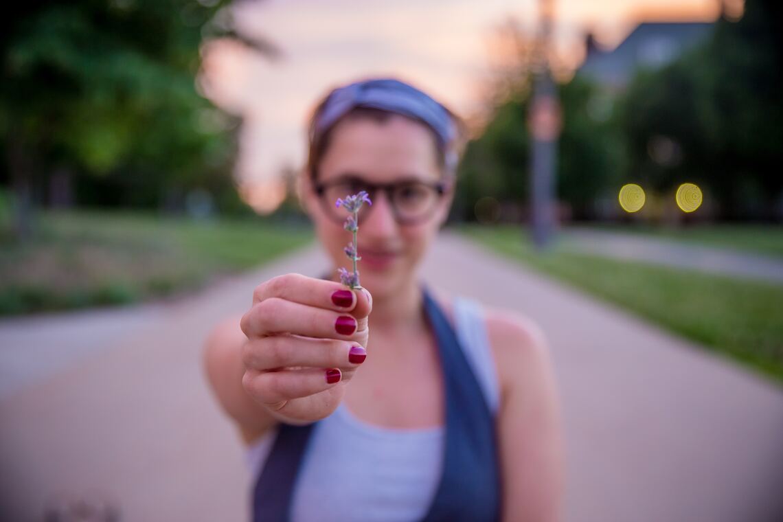 Smiling woman in park holding wildflower towards camera