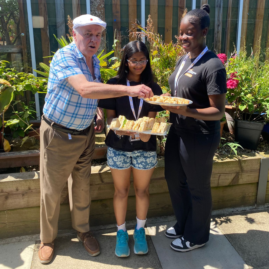 2 Young Commissioners holding trays of sandwiches, male guest helping himself to a sandwich